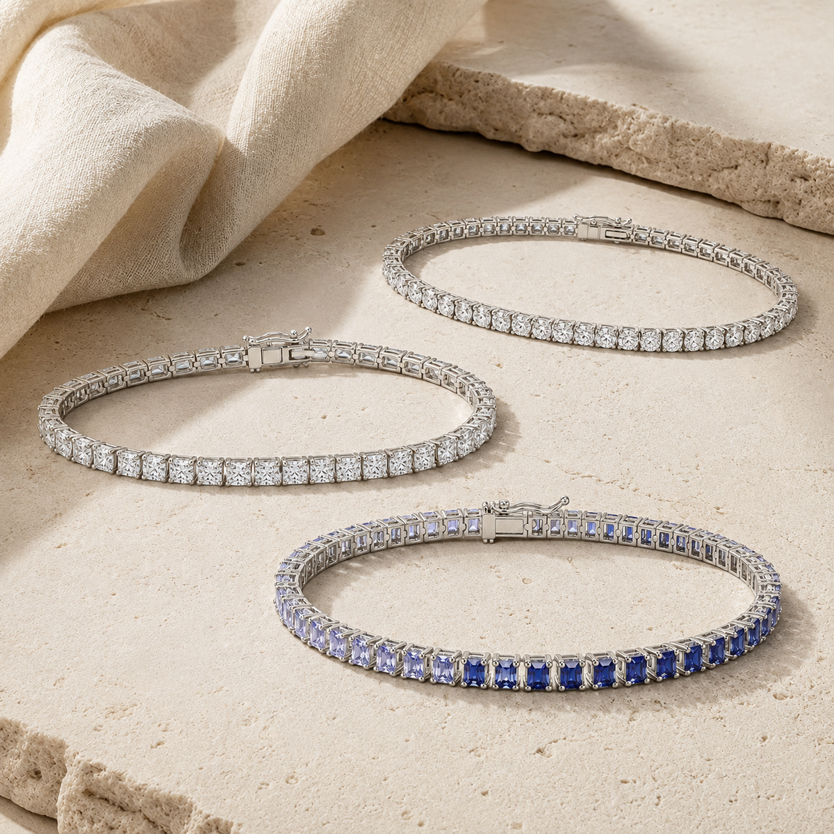 Three Myraé tennis bracelets with round, radiant and blue ombre stones on warm ivory limestone