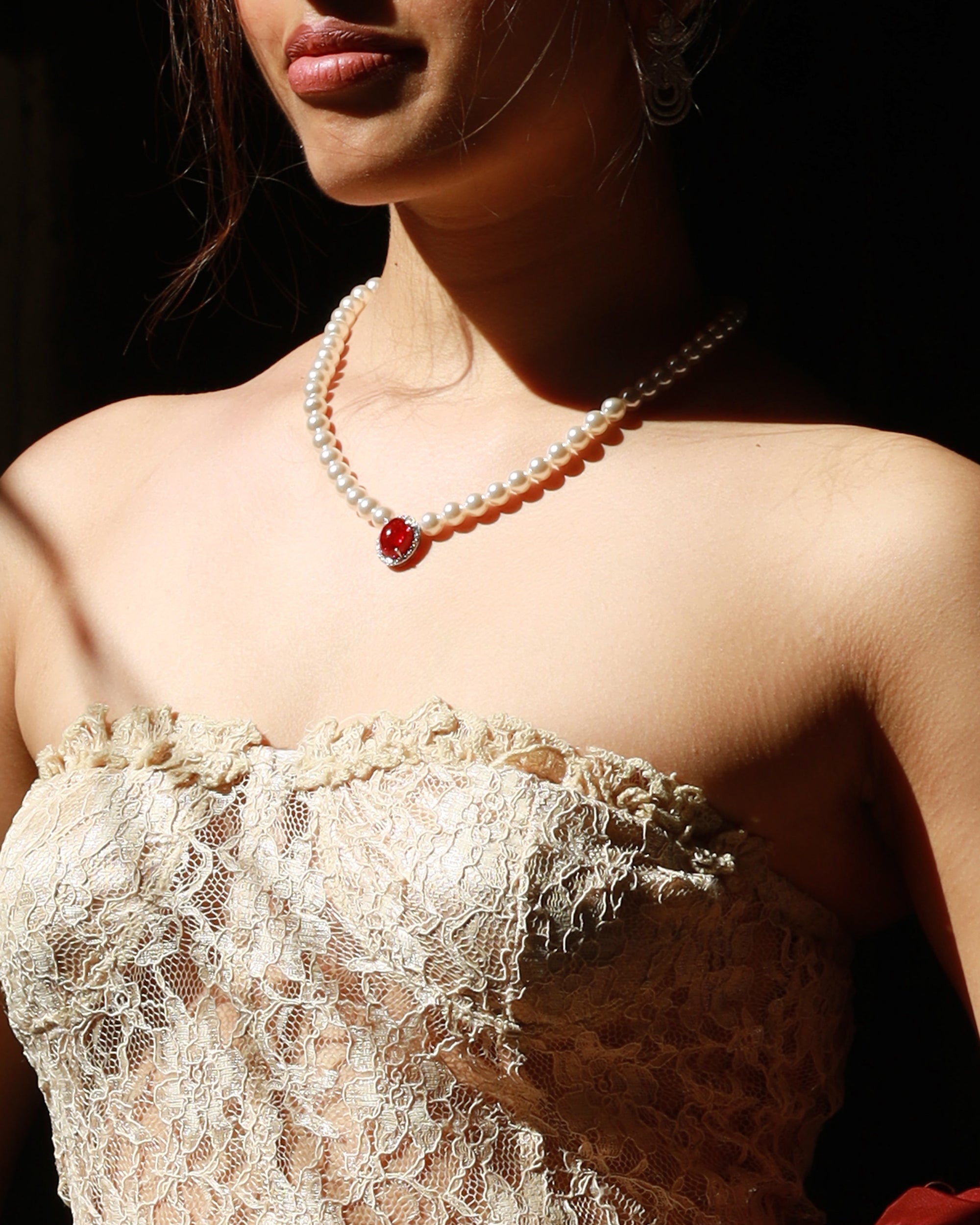 Woman wearing a lace top and red garment with a ruby necklace shown through a spotlight